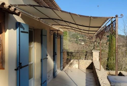 Toile de pergola beige imperméable installée sur structure en fer forgé, terrasse de maison en Provence