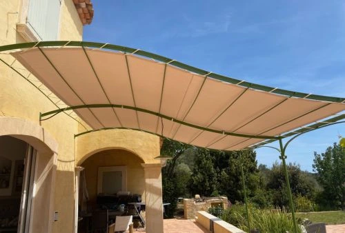 Toile de pergola beige ivoire sur structure métallique verte, protection solaire pour terrasse de maison provençale