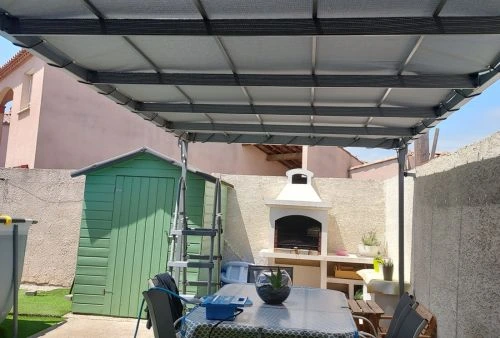Toile microperforée grise installée sur pergola en fer forgé, aménagement d’un coin repas extérieur